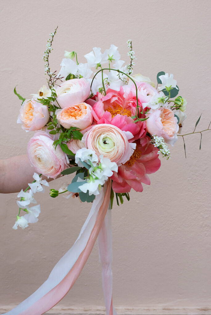 Ranunculus and peony bouquet against a light pink wall