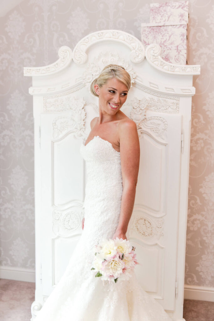 Pink dahlia wedding bouquet held by a bride in front of a white ornate wardrobe